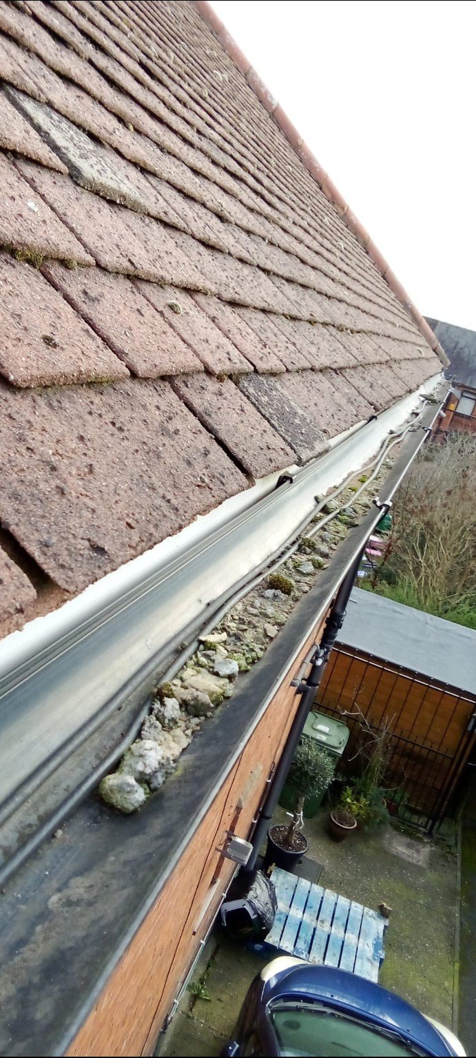 Heavy stones and moss blocking a roof gutter before RMS cleaning